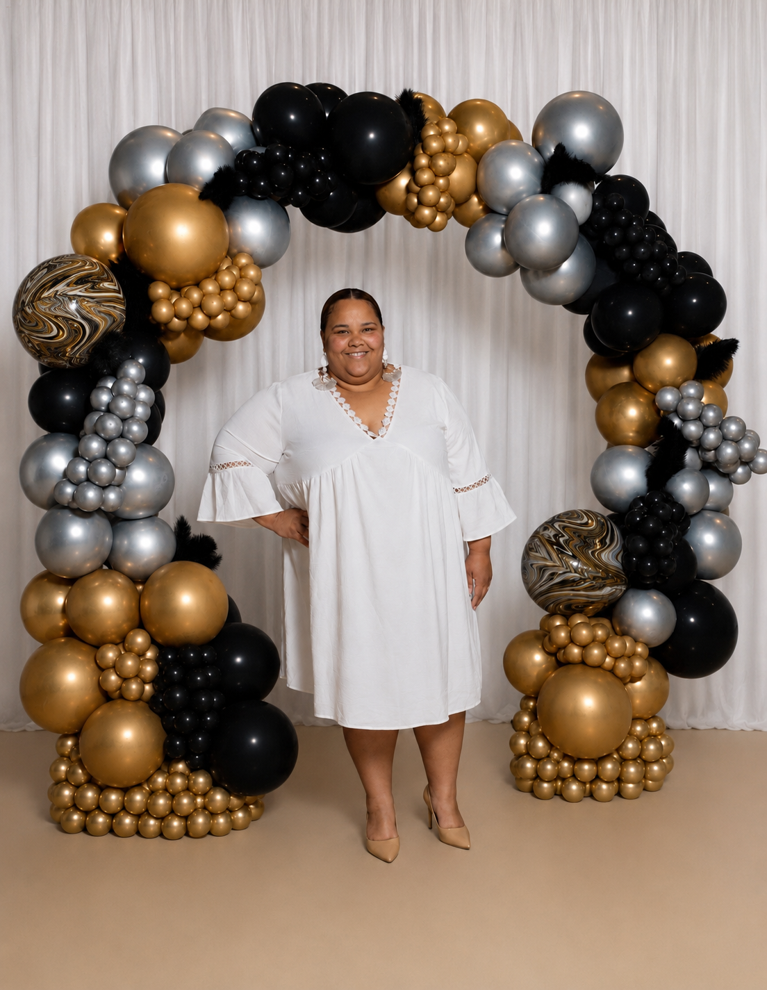 Liz Elliott standing inside a black, gold and silver balloon arch installation