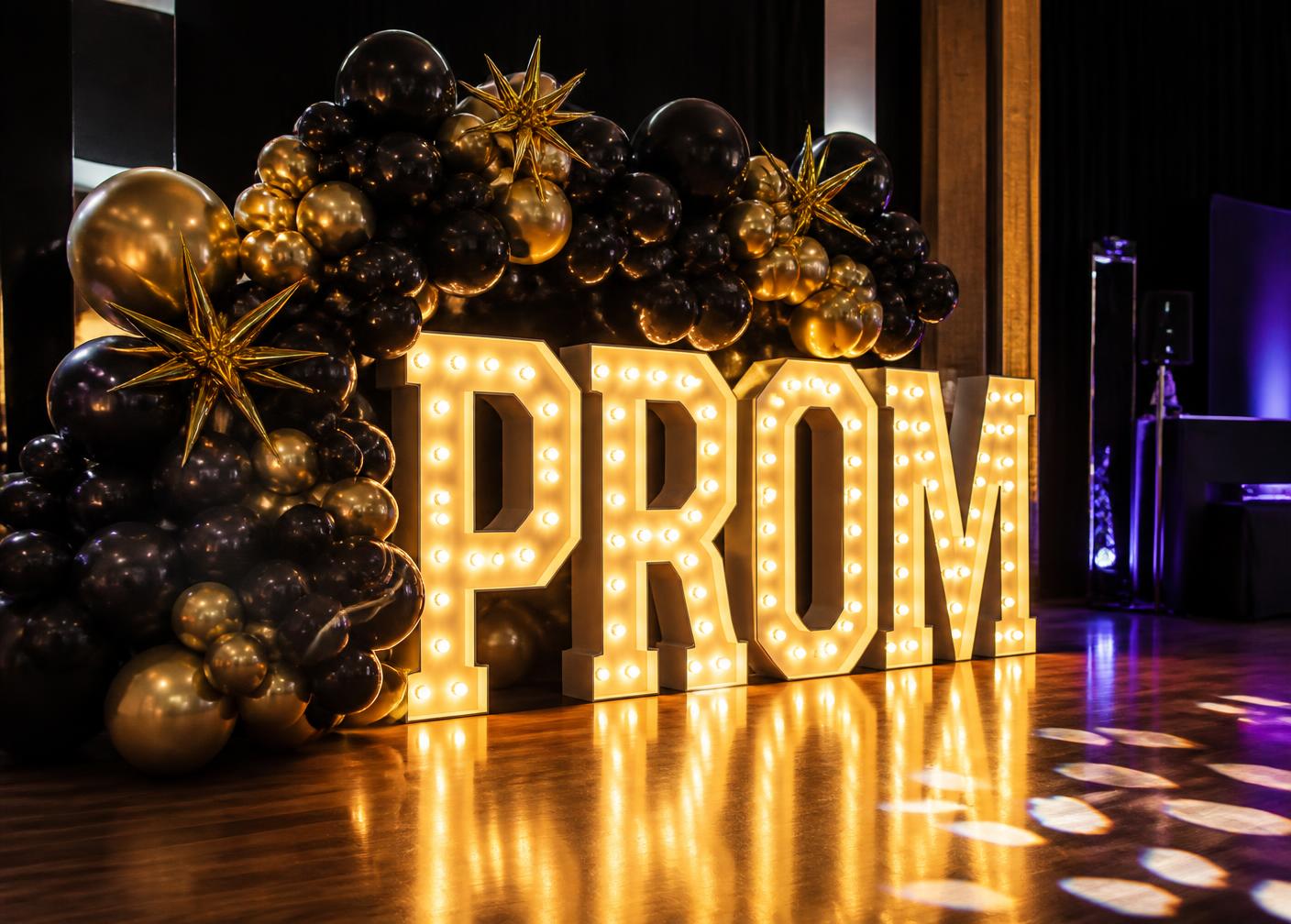 Illuminated PROM marquee letters framed by a black and gold balloon installation